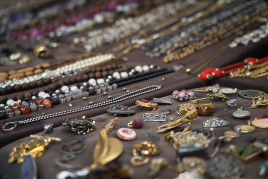 Vielf&auml;ltige Schmuckauslage auf dunklem Stoff, mit Ketten, Ringen, Armb&auml;ndern und Broschen in dichter, farbenreicher Anordnung. Detailreiches Markt‑ und Handwerksmotiv.