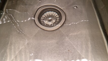 Water flowing in kitchen sink with drain in focus during daytime hours