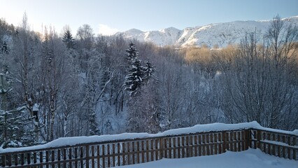 Snowy landscape with trees and mountains seen from a wooden deck