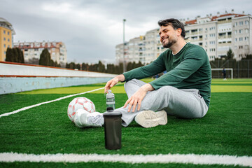 Adult man resting on soccer field with ball and bottle © Jelena