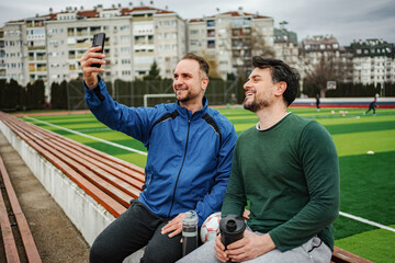 Adult men friends sitting on stadium bench taking selfie enjoying sport © Jelena