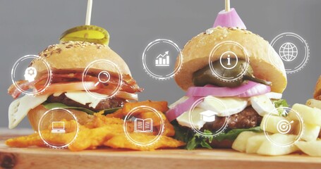 Showing two sesame slider burgers on wood board with fries, crinkle chips, skewers, HUD icons © vectorfusionart