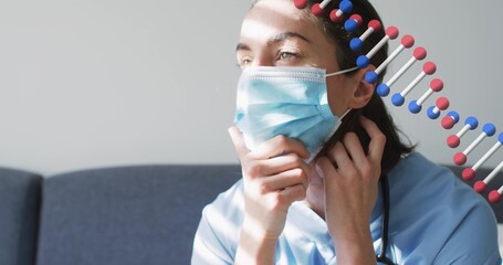 Adjusting scrub-clad nurse touching surgical mask and neck on couch with light bands, steth and DNA