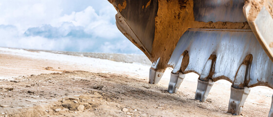 A powerful excavator bucket breaks ground on a sunlit day, sending dirt flying as it prepares the site for upcoming construction activities © Anoo