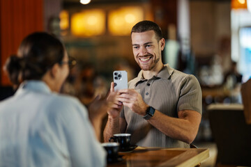 Man taking smartphone picture of woman in cafe