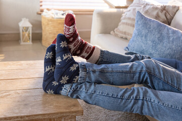 Couple reclining on sofa at home with legs on wooden table, wearing jeans and patterned socks