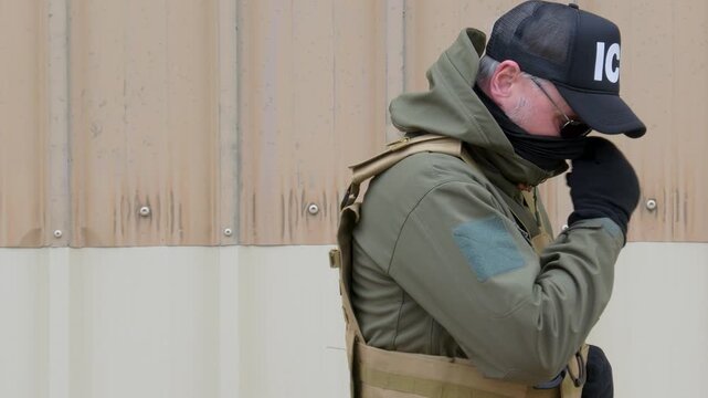An Immigration and Customs Enforcement (ACE) agent hides his face behind a mask.