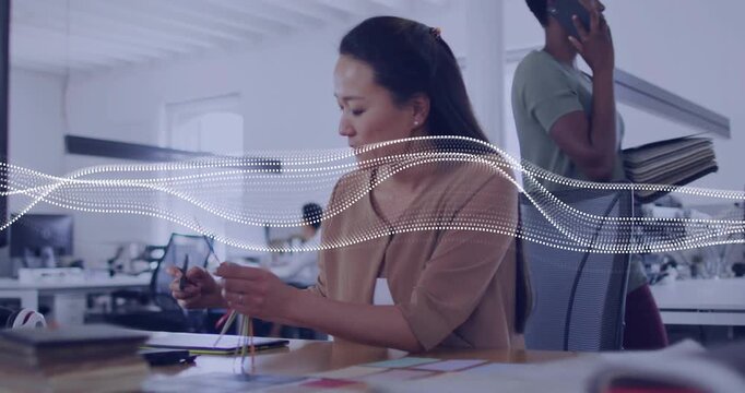 Midcareer woman sorting color cables in design, tapping device, noting, dotted waveform overlaying
