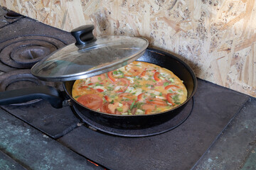 Fresh homemade omelette with tomatoes and herbs prepared in pan on old wood stove. Traditional cooking and countryside lifestyle concept.