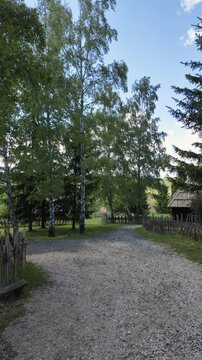 First person walk along a gravel path in ethno village Staro Selo in Sirogojno, Serbia. Peaceful rural atmosphere surrounded by wooden fences, trees and traditional architecture