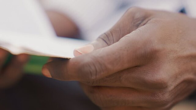 Black hands reading green booklet, closeup view of fingers turning pages, detailed skin texture and thumb grip, focused study moment, quiet intimate inspection of document, candid macro shot conveying