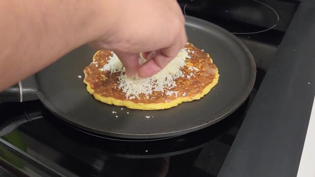 Man preparing Venezuelan cachapas with white cheese on flat pan.