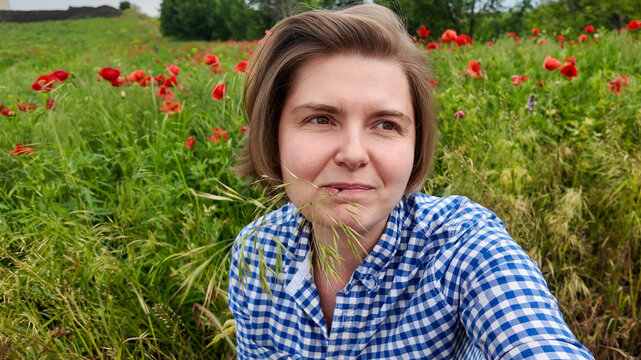 A pensive Caucasian woman in a gingham shirt among poppies, celebrating Lughnasadh, whispers of nature's untold secrets