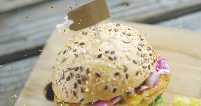 Showing seeded bun, sesame flax seeds, toothpick flag piercing patty, gold confetti on wooden board