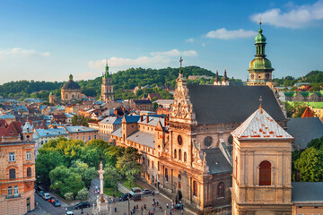 Obraz premium Aerial drone view of Lviv, Ukraine featuring historic churches, cathedral towers, and colorful rooftops in the old town city center. European cityscape with green trees and architectural landmarks see