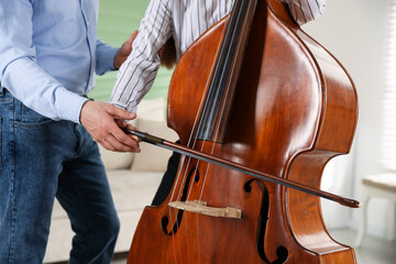 Fototapeta premium Girl learning how to play double bass with music teacher indoors, closeup