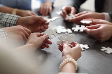 Obraz premium Team building. Group of businesspeople solving puzzle together at dark wooden table against light background, selective focus