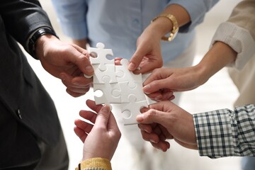 Obraz premium Team building. Group of businesspeople holding puzzle pieces together on blurred light background, closeup