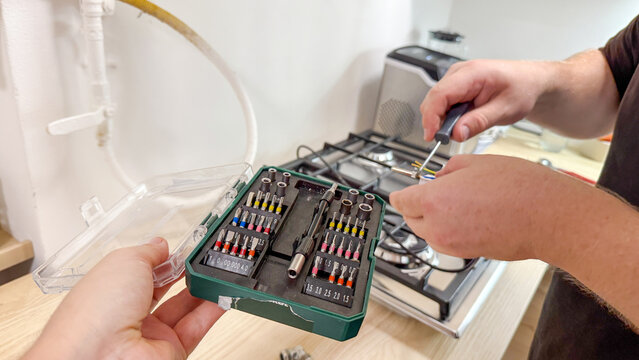 Silent kitchen tinkering unfolds as a Caucasian male's hands orchestrate a delicate screwdriver ballet; reminiscent of DIY Day
