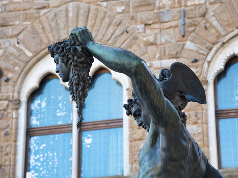 Perseus Holding Medusa's Head Close-up - Detail of Cellini's bronze sculpture showing the decapitated head of Medusa and Perseus's arm against the blurred stone facade of Palazzo Vecchio.