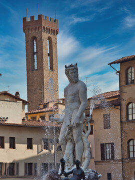  Vertical close-up of the white marble Neptune statue with water spray, set against the historic stone tower of the Bargello Museum and Renaissance buildings.