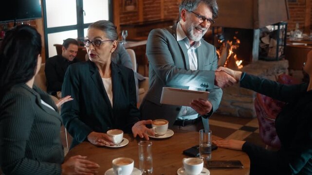 Handshake during business meeting in restaurant over coffee. Group of business people negotiating strategy and reaching agreement through collaboration