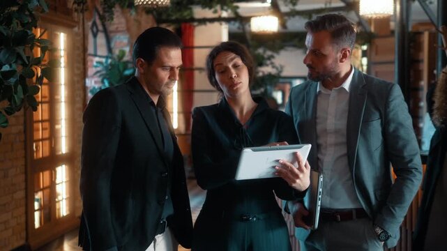 Real estate agent presenting property details on tablet to investors or buyer before touring luxury hotel interior. Business inspection and investment consultation.