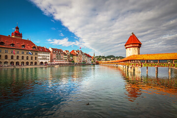 Obraz premium Beautiful view of Lucerne, Switzerland featuring the famous wooden Chapel Bridge with Water Tower over the Reuss River. Scenic cityscape with alpine mountains, clear water, and colorful historic archi