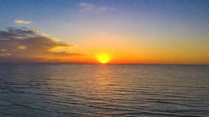 Naklejka premium Bright sun lowering above tranquil ocean with gentle ripples.