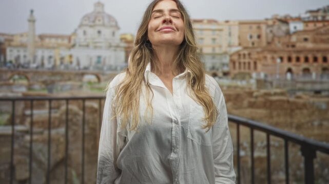 Woman eyes closed, head tilted back showing face and neck, wearing white shirt, hands relaxed at sides, standing by railing overlooking ruins at building; serenity travel contentment.