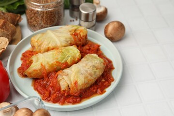 Yummy stuffed cabbage rolls and ingredients on white tiled table, closeup. Space for text