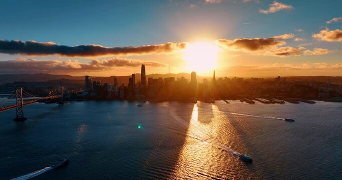 Motor boats move by the bay waterscape at sunset. Setting sun lights the skyline of San Francisco, California, USA.
