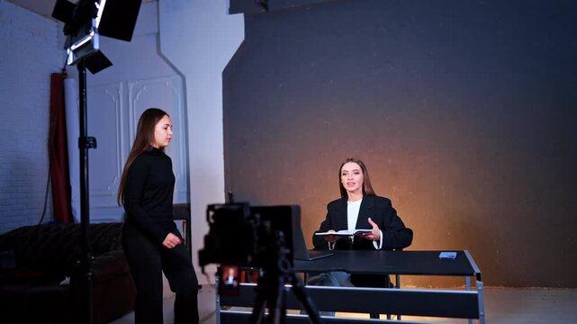 Photographer's assistant passes the book to a lady sitting at desk. Studio footage of program or blog.