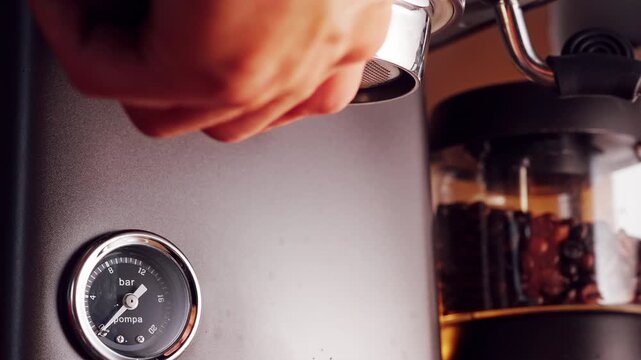 Barista installing bottomless portafilter into espresso machine group head, close up view with pressure gauge and grinder hopper visible, professional coffee preparation workflow