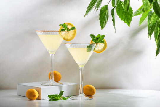 Bright and refreshing cocktail with two glasses of limoncello spritz, garnished with fresh lemon slices and mint sprigs on a white surface, with green foliage in the background