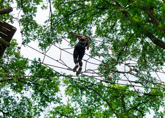 Young girl climbing rope course in forest adventure park