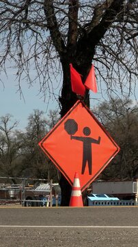 Flagman ahead sign on side of highway with passing vehicles, in vertical format.