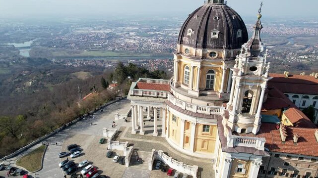 High angle drone shot shows the majestic Basilica of Superga with its grand dome and classical portico on the hilltop in Turin, Italy, historic baroque architecture, city panorama, sunny daylight.