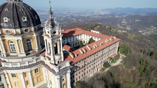 High angle drone shot reveals the majestic Basilica of Superga with its grand dome and classical portico on the hilltop in Turin, Italy, historic baroque architecture, city panorama, sunny daylight.