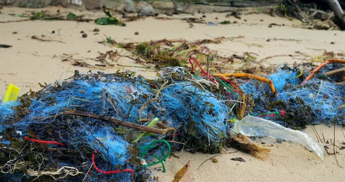 Blue net entangled with plastic bottle on sand, close perspective shows filaments and fragments, gritty texture of debris, stark representation of microplastic threat and marine entanglement risks