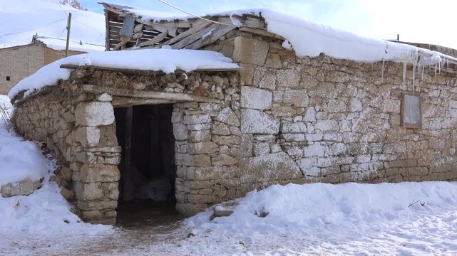 Ancient stone house covered in snow located in rural village of Pakistan during winter season. Traditional rustic dwelling with weathered walls and primitive architecture in remote mountainous region.