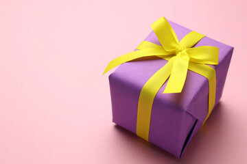 Obraz premium Wrapped gift with bow on light pink background, closeup. Space for text