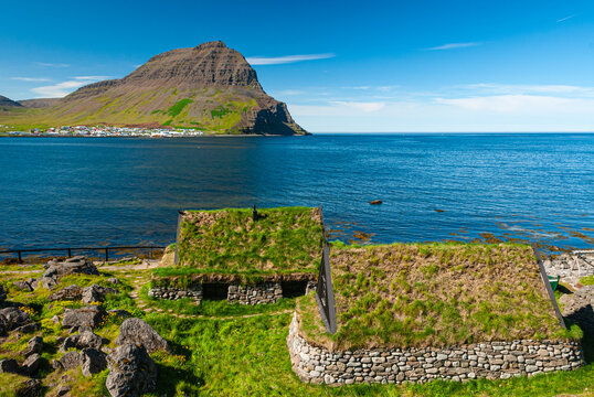 Traditional turf houses at &Oacute;sv&ouml;r maritime museum in Iceland, historic fishing huts with grass roofs overlooking the Atlantic Ocean on a sunny summer day.