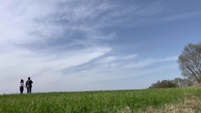 a loving couple walking through a field in summer