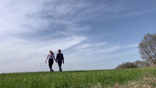 a loving couple walking through a field in summer
