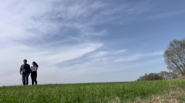 a loving couple walking through a field in summer