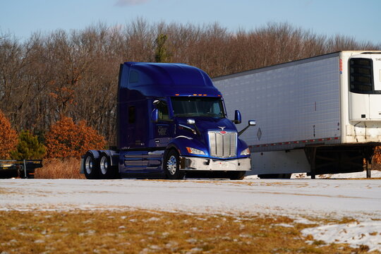 Blue semi truck tractor parked on snowy ground by trailer. Professional logistics, freight transport, and winter shipping industry concept.