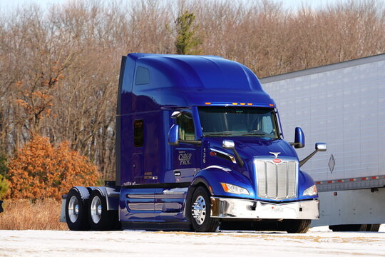 Blue semi truck tractor parked on snowy ground by trailer. Professional logistics, freight transport, and winter shipping industry concept.