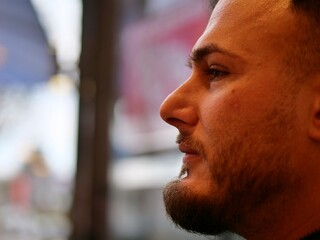 Profile portrait of a bearded man with cinematic warm lighting and deep shadows. Close-up of a masculine face in a cafe or urban setting. Moody expression, thoughtful look, and groomed facial hair.  © Ena