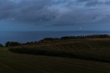 Fototapeta premium A cloudy sky with a red full moon in the background above the sea.